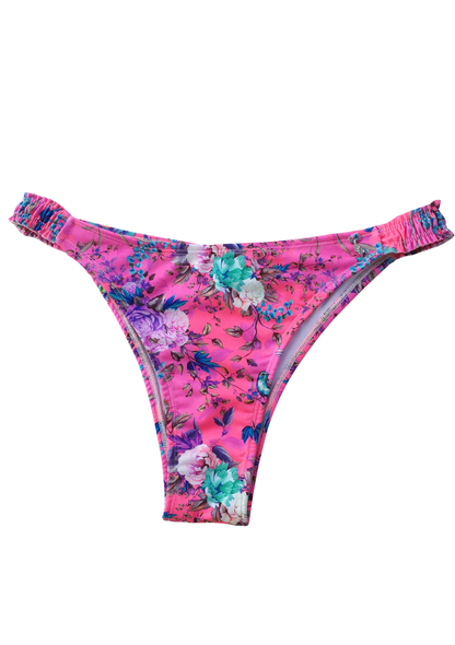 Bombacha de bikini colaless cavada con estampado de flores sobre fondo rosa fucsia y detalle elástico fruncido en los costados.